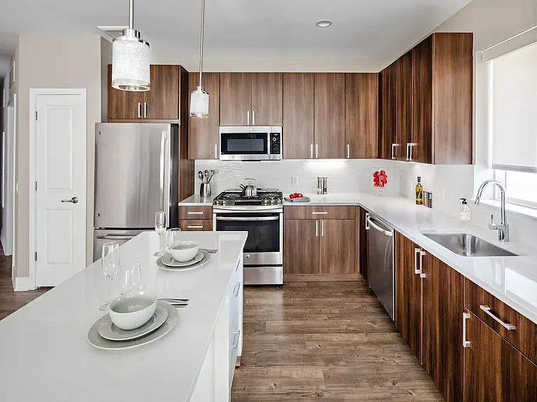Signature Collection Kitchen with oak cabinetry, light grey quartz countertops, white tile backsplash, upgraded stainless steel appliances, and hard surface plank flooring