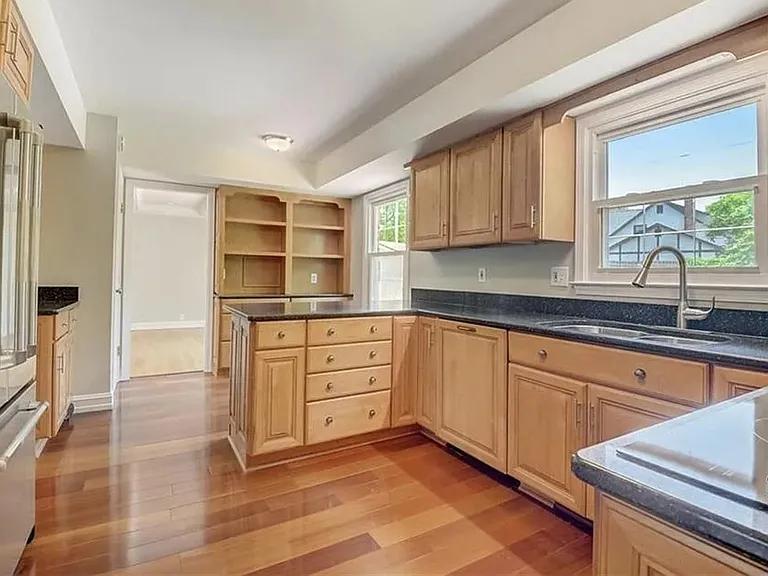 Spacious kitchen with ample wood cabinetry, open shelving, stainless fridge, and generous counters with a windowed sink.