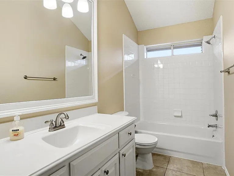 Bathroom featuring a white vanity with integrated sink, brushed nickel faucet, framed mirror, and a combination tub/shower with white subway tile surround and an inset window
