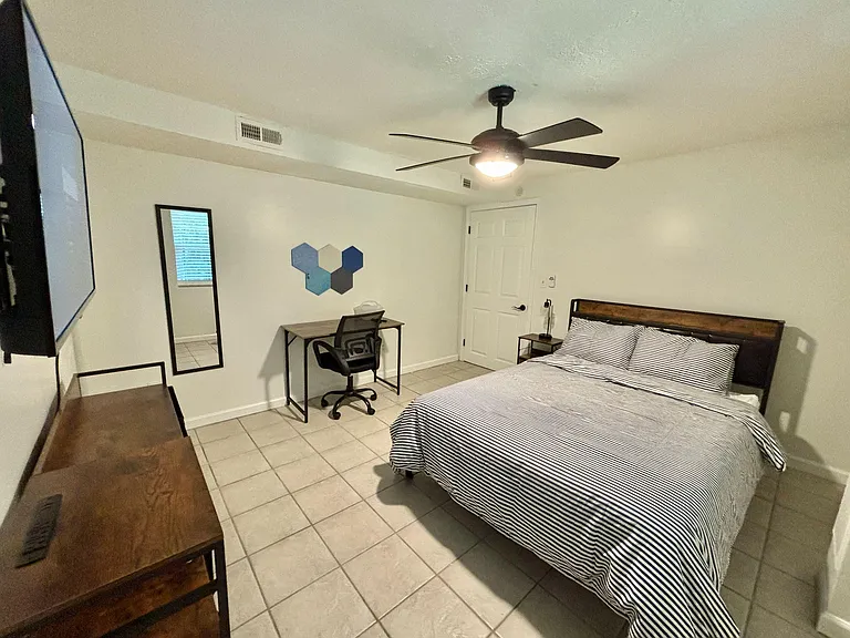 Furnished bedroom with tile floors, ceiling fan, TV, and a dedicated desk area for work or study.