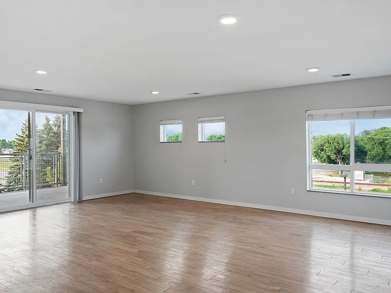 Bright and spacious living area with hardwood floors, featuring large windows and a sliding door opening to a balcony with views of lush greenery. Bright and spacious living area with hardwood floors, featuring large windows and a sliding door opening to