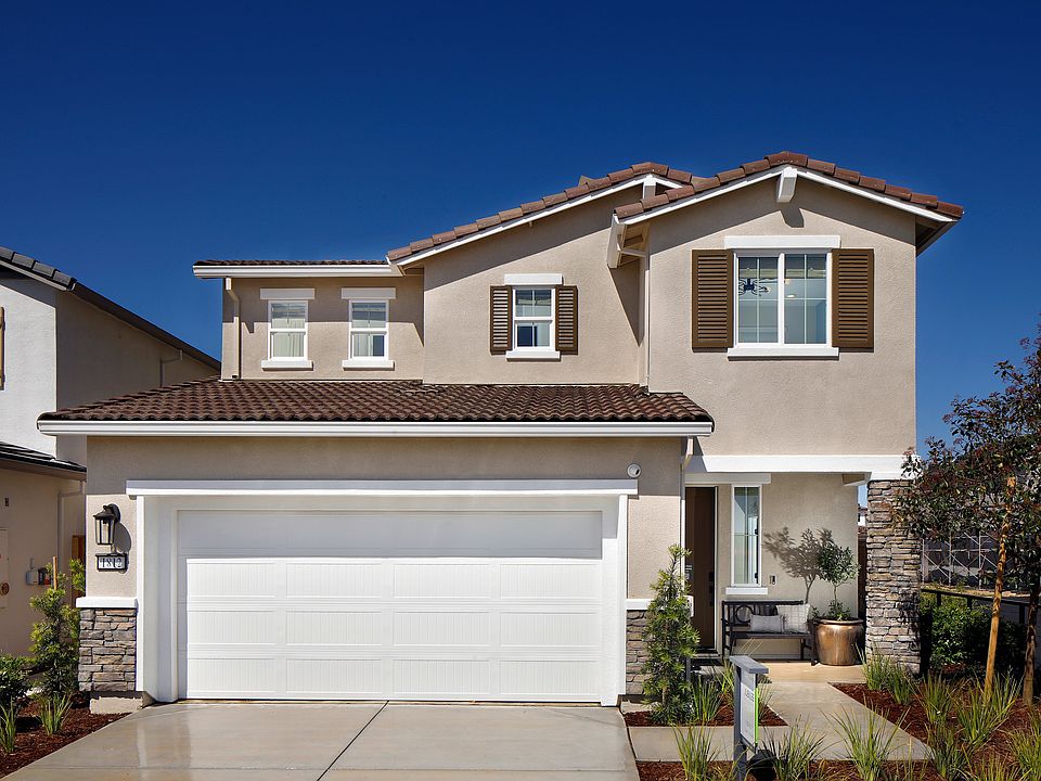 A two-story residential house with a garage door, surrounded by landscaping and a clear blue sky in