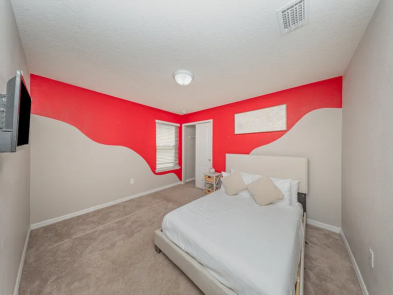 This bedroom features bold accent walls and a comfortable bed setup. A mounted TV and closet space add convenience.