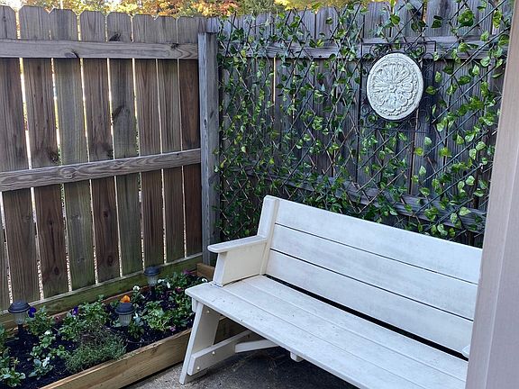 Back patio. Raised bed planter for flowers or small herb garden. Green vine cover on the right side is not present. Edison string lights are installed.