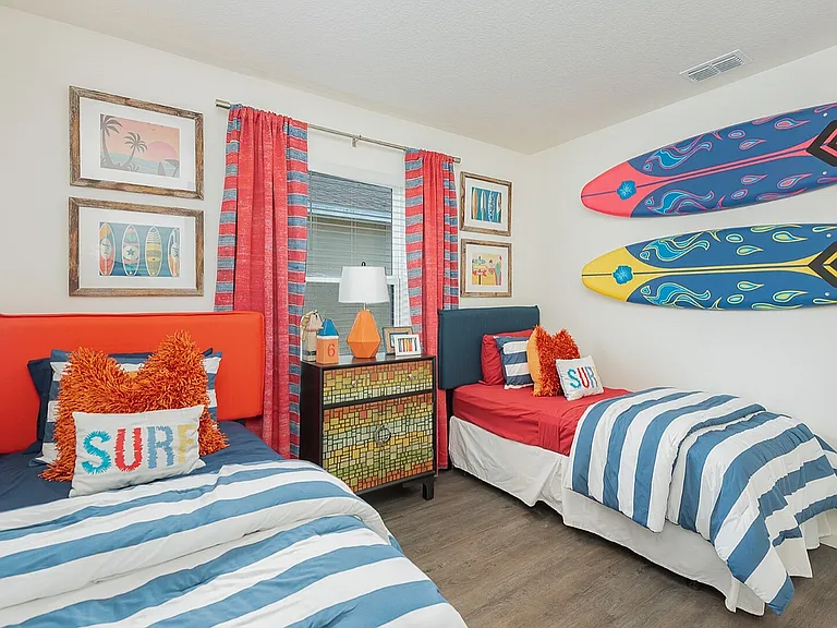 Vibrant nautical-themed bedroom with two cozy twin beds adorned in blue and white stripes, surfboard wall decor, and colorful ocean-inspired accents.