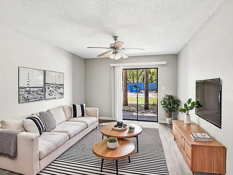 Bright and airy living room featuring a cozy beige sofa, stylish striped rug, and modern entertainment center, with large sliding glass doors leading to a peaceful outdoor view.