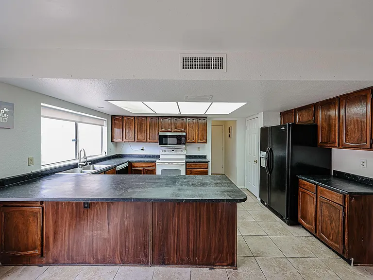 Spacious kitchen with ample wood cabinetry, large breakfast bar, black countertops, and full appliance set.