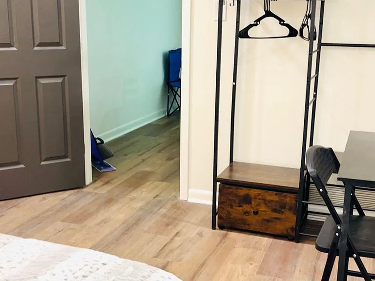 Private bedroom with wood-look flooring, a comfortable bed, and a workspace plus open clothing rack for easy storage.