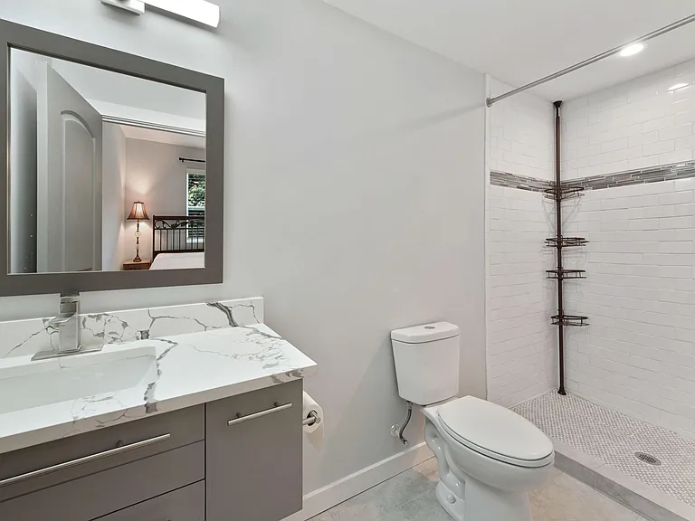 Updated bathroom with a large tiled walk-in shower, single-sink vanity with stone-look countertop, and ample storage.
