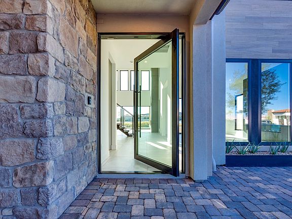 A glass-paneled entryway leads into a modern, open-concept interior, with a stone wall and a brick p