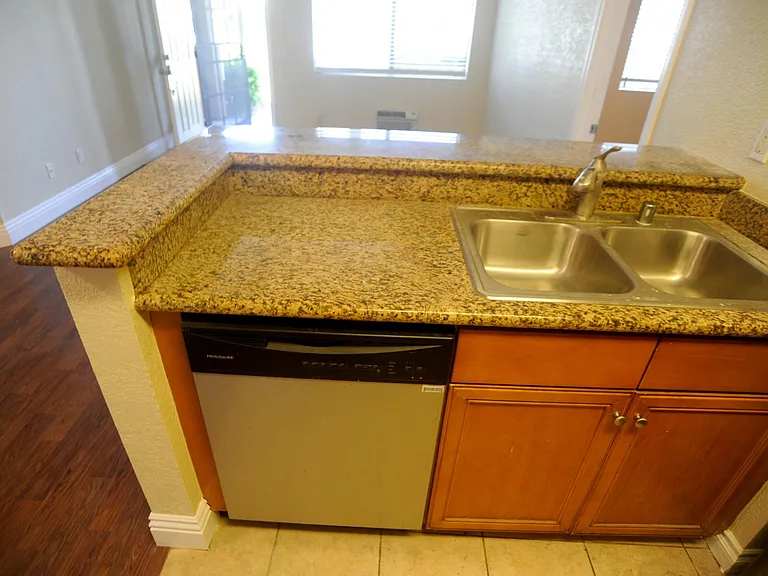Stainless steel dishwasher and granite counter- top looking out over open space living / dining area