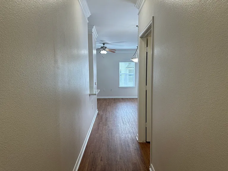 Bright hallway with elegant wood-style flooring leading to a spacious living area, accented by a ceiling fan and large window. Bright hallway with elegant wood-style flooring leading to a spacious living area, accented by a ceiling fan and large window.
