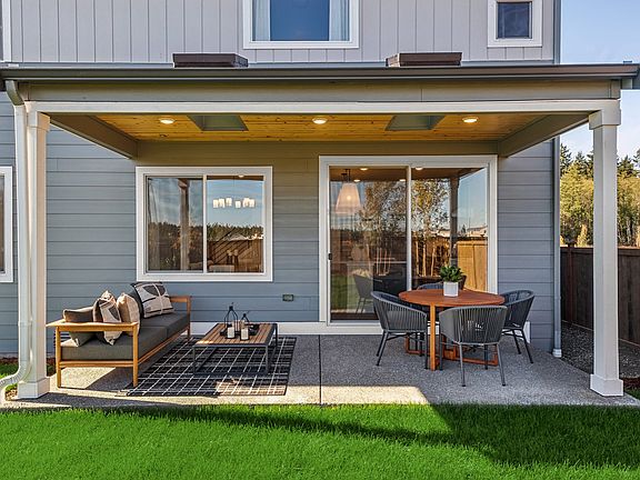 A cozy outdoor patio with a covered seating area, surrounded by a well-manicured lawn and a modern,