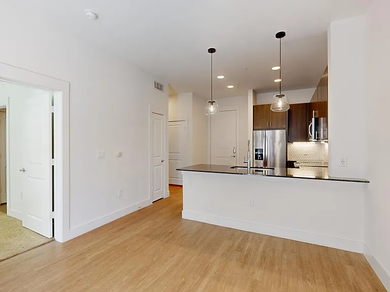 Apartment kitchen with stainless steel appliances, dining and living room with wood-style flooring.
