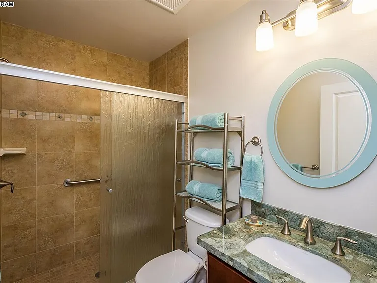 Guest bath in hallway between two guest bedrooms. Large tiled walk-in shower with glass doors. Vanity and medicine cabinet.