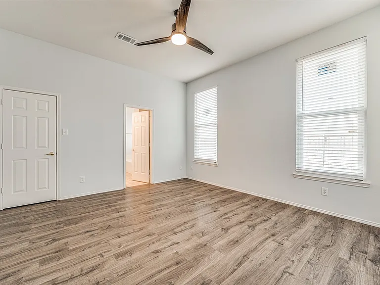 Spacious room featuring wood-finish flooring, white walls, and a vaulted ceiling with a ceiling fan