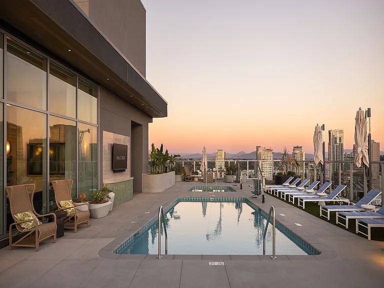 Luxurious rooftop pool deck at sunset with stunning city skyline views, stylish loungers, and elegant seating.