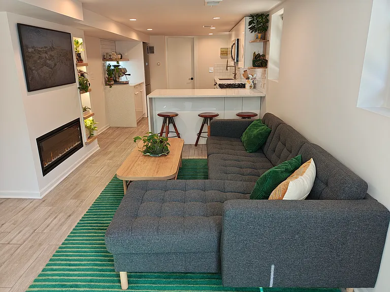 The living room has an electric fireplace and bar seating for three at the kitchen island. The TV is a frame TV that shows art.
