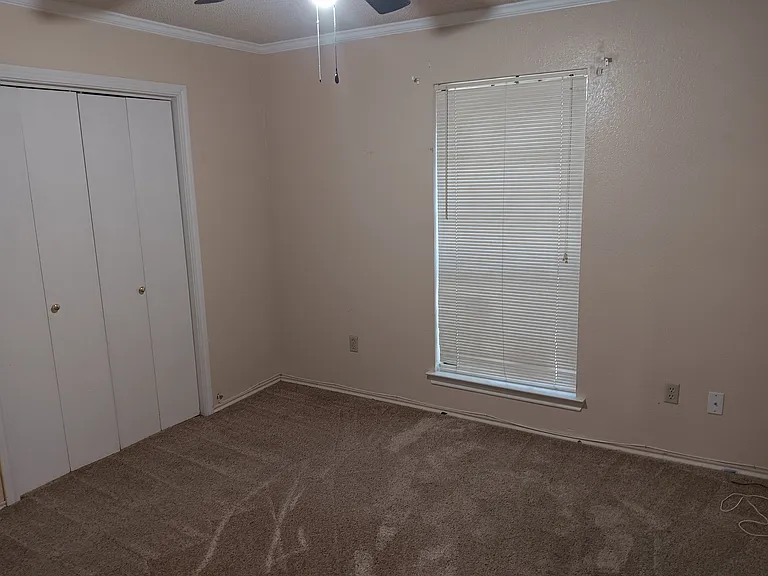 Bedroom 2 with ceiling fan, crown moulding, plush carpet, wall closet space with light.