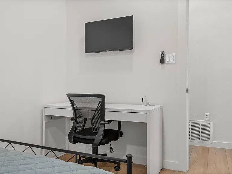 Bedroom work area with a dedicated desk, rolling chair, and wall-mounted TV for relaxing or remote work.