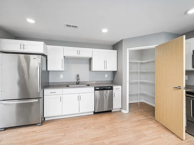 Modern kitchen with stainless steel appliances, white cabinetry, and walk-in pantry, featuring sleek wood flooring. Modern kitchen with stainless steel appliances, white cabinetry, and walk-in pantry, featuring sleek wood flooring.