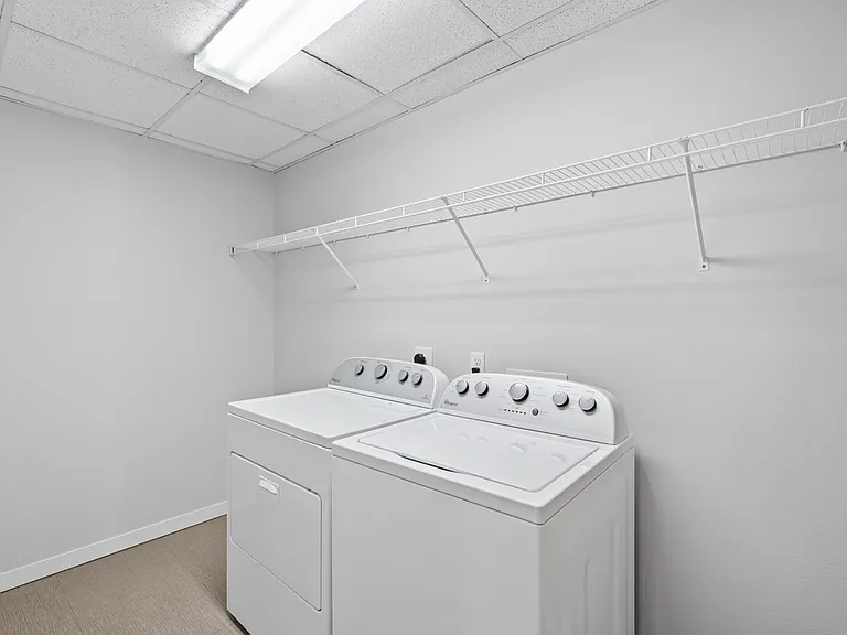 Bright and spacious laundry room featuring modern washer and dryer, complemented by an overhead wire shelf for convenience. Bright and spacious laundry room featuring modern washer and dryer, complemented by an overhead wire shelf for convenience.