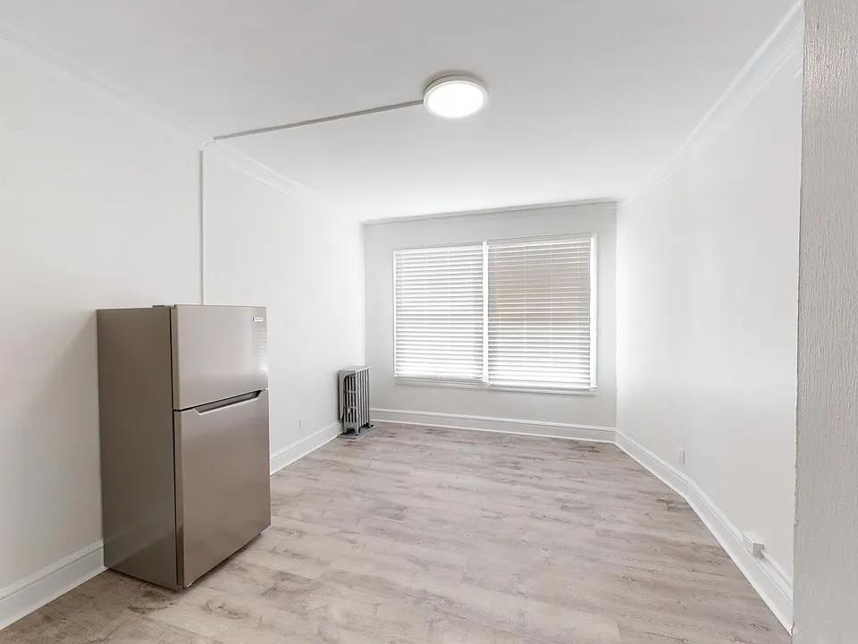 Living area with a wood-like flooring, a large window and a refrigerator
