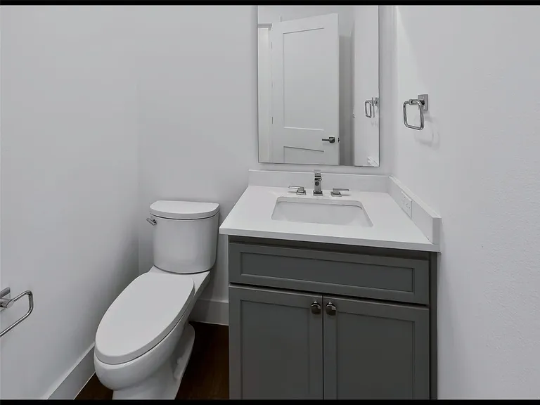 Modern bathroom featuring a single white toilet, a vanity with a gray cabinet, white countertop, an undermount sink, and a framed mirror