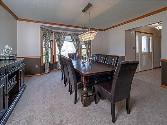 An elegant dining room features a bright bay window, chair rail, neutral tones, crown molding and a striking chandelier.