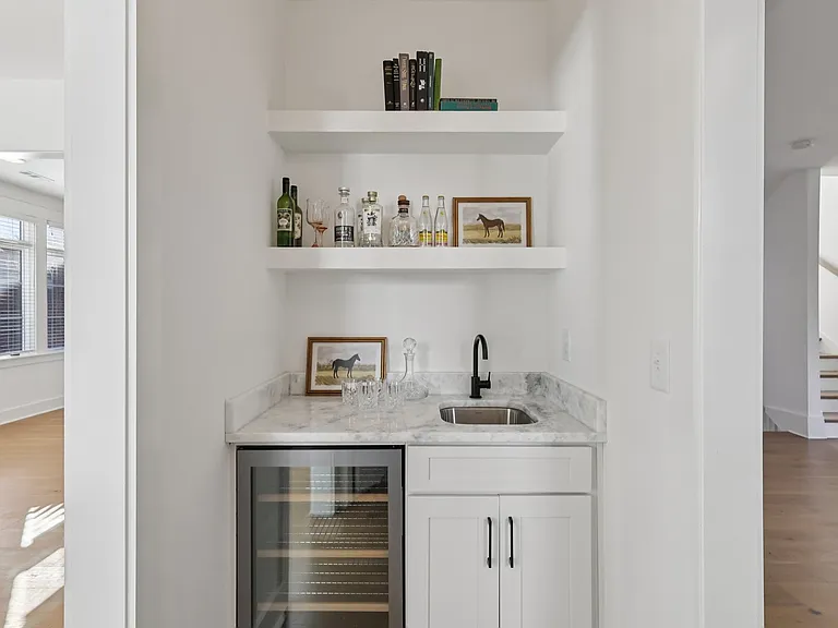 Built-in wet bar with beverage refrigerator, marble countertop, and open shelving.