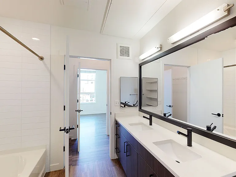 Apartment bathroom with large soaking tub, wood-style flooring and double sinks.