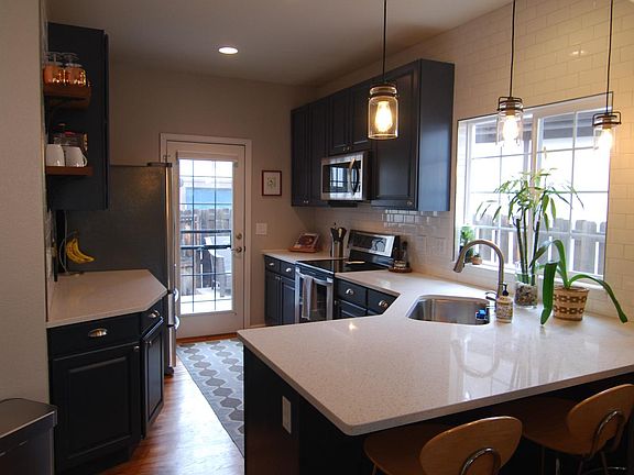 Fully tiled backsplash, quartz countertops, deep sink with rack, and accent shelving.