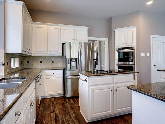 Kitchen featuring wood-finish flooring, white cabinetry, a double basin sink, and built-in stainless steel appliances, including a refrigerator and double ovens