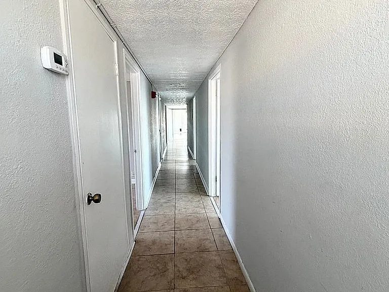 Bright, spacious hallway with modern tile flooring and sleek white walls leading to cozy rooms.