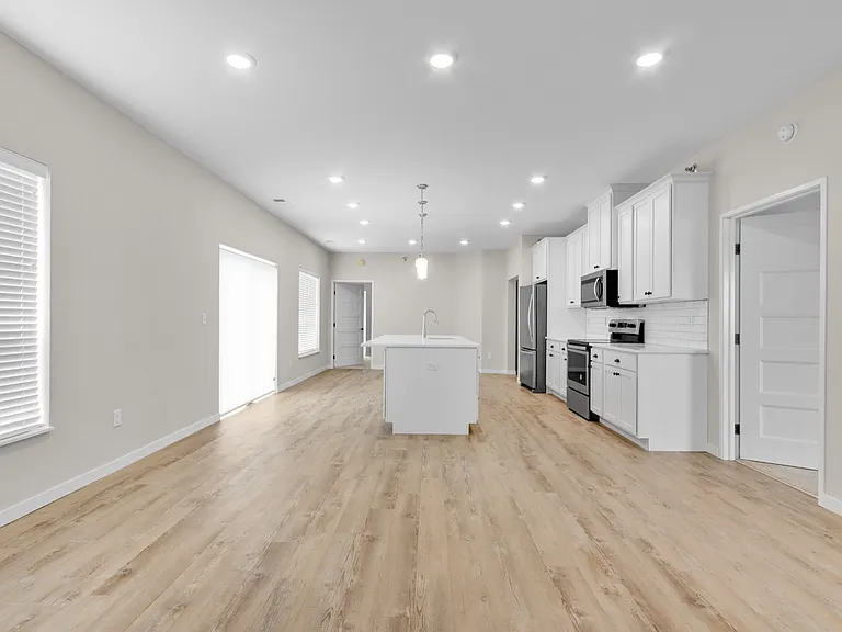 Modern open-plan kitchen and living area with sleek white cabinetry, central island, and stylish wood flooring. Modern open-plan kitchen and living area with sleek white cabinetry, central island, and stylish wood flooring.