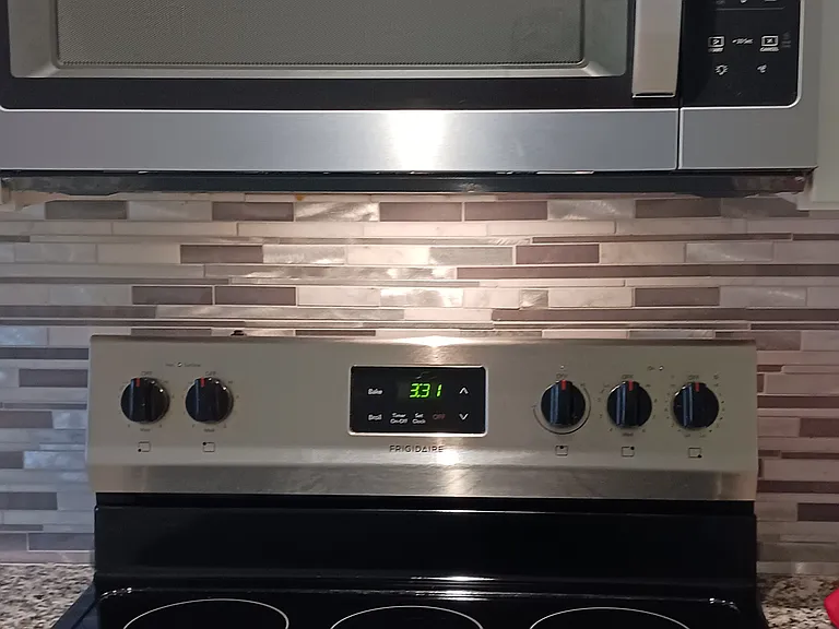 Stove and microwave with backsplash tile that has stainless steel accents