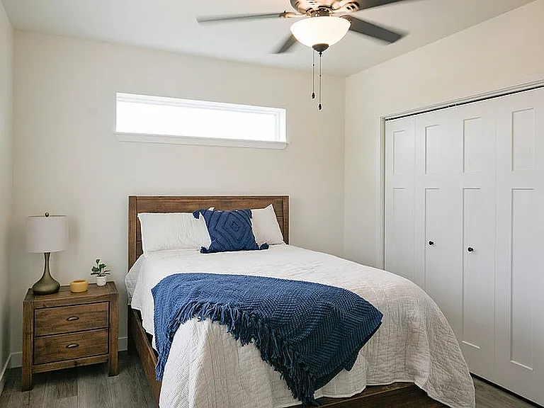 Bright and cozy bedroom featuring a comfortable bed with a navy throw, modern nightstand, and ample natural light from the window above.