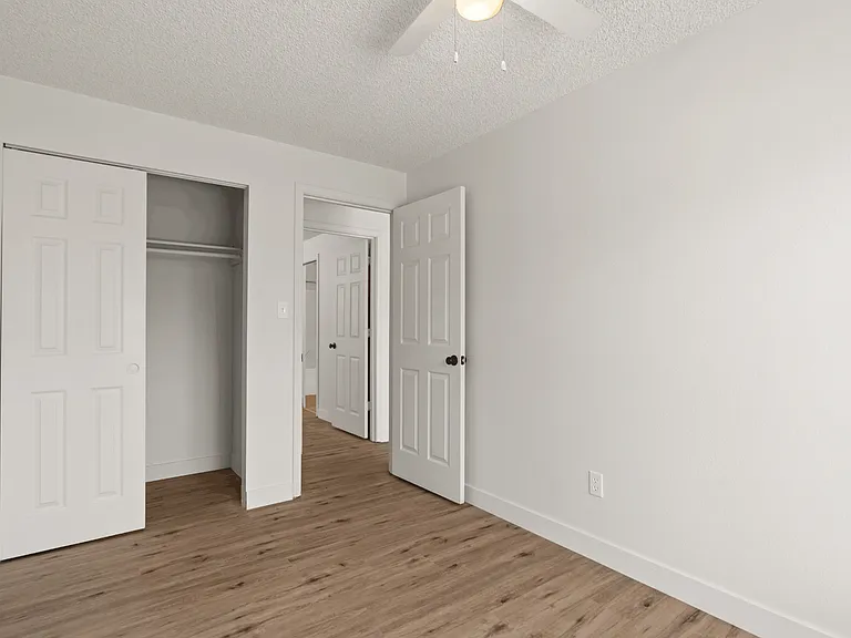 Inviting bedroom offers space for a large bed, a ceiling fan, wood-style flooring, and a roomy closet with shelving and hanging storage. Inviting bedroom offers space for a large bed, a ceiling fan, wood-style flooring, and a roomy closet with shelving an