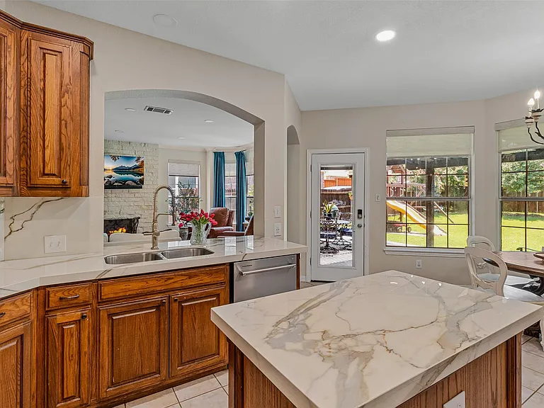 Chef's kitchen featuring wood cabinetry, white stone countertops with integrated sink, stainless steel dishwasher, and an island with a matching stone countertop