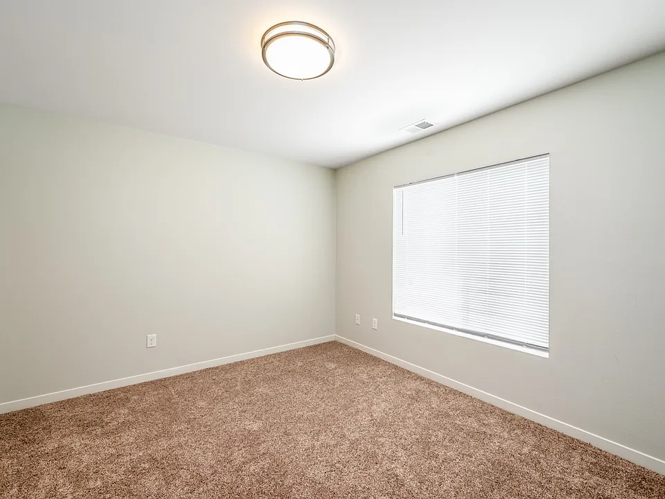 Bright and cozy empty room with soft carpeting, modern ceiling light, and large window with blinds. Bright and cozy empty room with soft carpeting, modern ceiling light, and large window with blinds.
