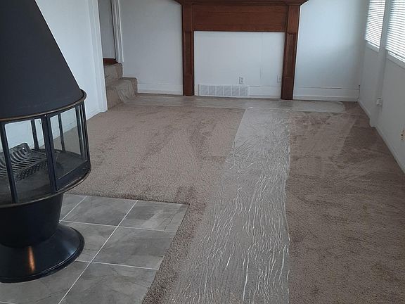 View of family room with woodburning fireplace, from far north end of room. Back door that accesses fenced backyard is out of view. Full bank of windows to right in photo look out on Arkansas River. Two steps lead into utility room, and door into garage