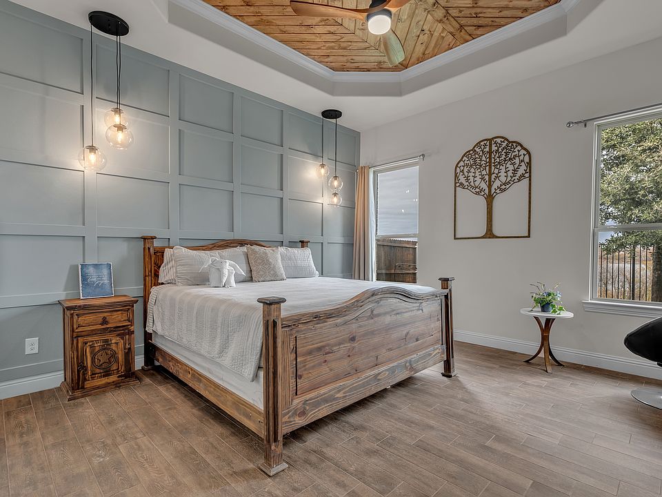 Master bedroom with a king bed, with backyard views of the lake and sunsets, light-blocking curtains as well, a dresser, a sitting area, side tables, a ceiling fan, and side tables with drop-down pendant lamps. All tile floor.