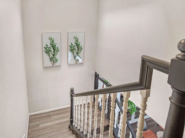 Open stairwell with updated railings, durable wood-look flooring, and wall art accents connecting the home's levels.