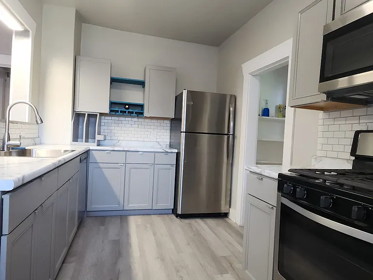 Another view of the kitchen showing premium vinyl plank flooring, some custom features, stainless steel fridge, range and microwave, with a glimpse into the walk-in pantry.