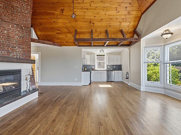 The bright and airy living room features vaulted wood-plank ceiling with exposed beams, big bright windows from every angle, bay windows, working fireplace, and original hardwood flooring.