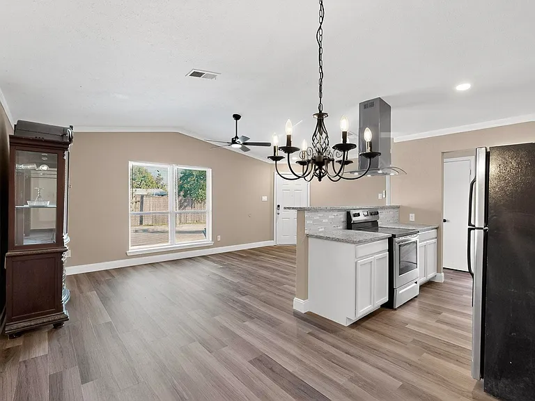 Kitchen featuring appliances with stainless steel finishes, white cabinetry, a chandelier, open floor plan, and light stone countertops