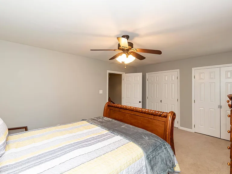 Bedroom features a ceiling fan with light, neutral walls, carpeted floors, and double-door closets for ample storage.