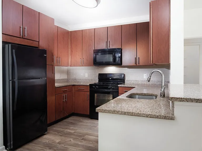 Classic Package kitchen with oak cabinetry, brown laminate countertops, beige tile backsplash, black appliances, and hard surface plank flooring (in select homes)