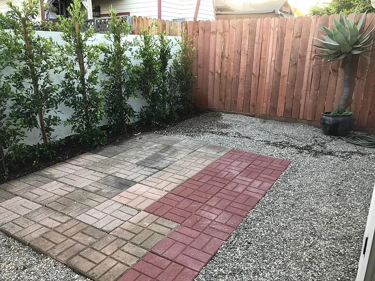 A view of the back yard with a new hedge and gravel. The pavers provide an area for relaxing or dining al fresco.