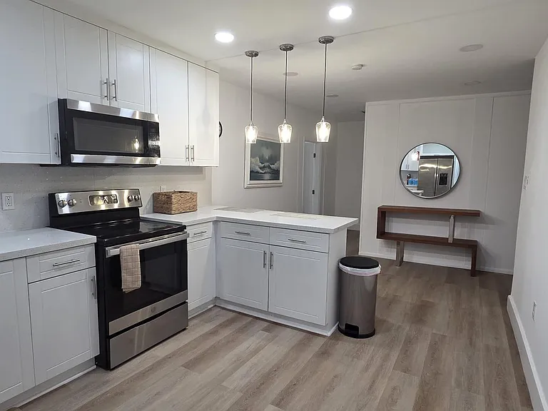 Spacious kitchen with white shaker cabinetry, stainless steel range and microwave, and a large peninsula with pendant lightin
